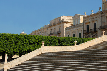 view from the great staircase of the Cathedral  of the baroque city of Noto in the summer light of Sicily and the golden stone that shapes every shape.
