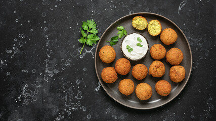Falafel balls with sauce on a black stone background. Top view, flat lay.