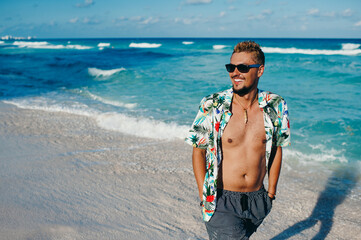 Young tourist man wearing hawaiian shirt at the sea or the ocean background. Travel vacation holiday. Man walking at the sea, enjoy tropical season - obrazy, fototapety, plakaty