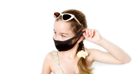 Happy little girl takes off her covid-19 protective medical black mask from her face in a beach suit outdoors. The concept of defeating the coronavirus.