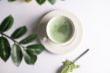 A white porcelain cup with japanese matcha tea drink on a white saucer plate on a white surface, a...