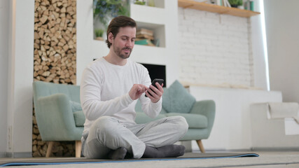 Young Man using Smartphone on Excercise Mat at home