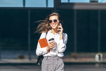 Business woman walking and talking on the cellphone outdoors near modern business center with...