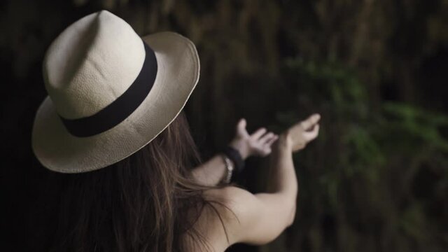 Young women's with fashionable hat exploring a cave and catching dripping water from its rocks.