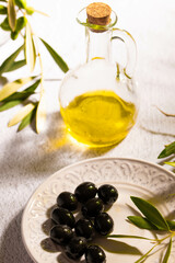 A glass jar with virgin olive oil, textured plate with black olives and a branch of olive tree