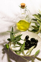 A glass jar with virgin olive oil, textured plate with black olives and a branch of olive tree