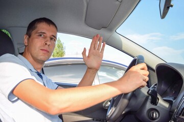 
On a summer day on the road, the driver of a car behind the wheel waves to another driver
