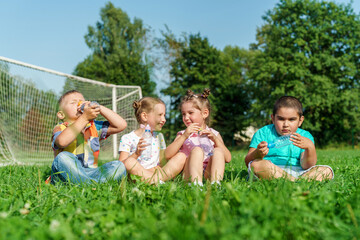 Obraz premium Small children, preschoolers drink water sitting on grass in park on sunny summer day. Outdoor games in fresh air. fun childhood. An active game. Water balance. children are very thirsty.