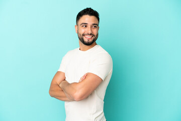 Young arab man isolated on blue background with arms crossed and happy