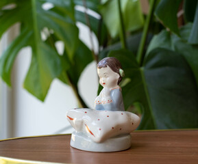 Vintage ceramic figurine - praying gearl in pajama with a pillow - on a wooden table with plants in the background