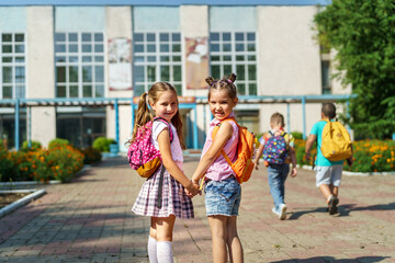 Two girls, elementary school students with backpacks, walking down street Happy children are returning to school. beginning of school year. Children in full growth, happily went to school. rear view