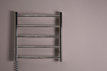 Modern heated towel rail on grey wall. Space for text