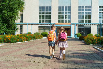 Two girls, elementary school students with backpacks, walking down street Happy children are returning to school. beginning of school year. Children in full growth, happily went to school. rear view