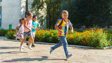 Naklejka premium group of school children with backpacks run out of school, after the end of classes. Classmates, school friends. The beginning of holidays. The end of quarantine. Back to school.