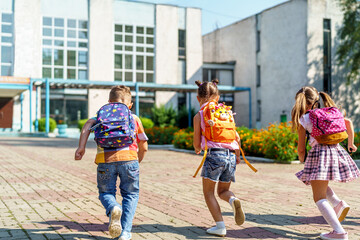 group of school children with backpacks run out of school, after the end of classes. Classmates,...
