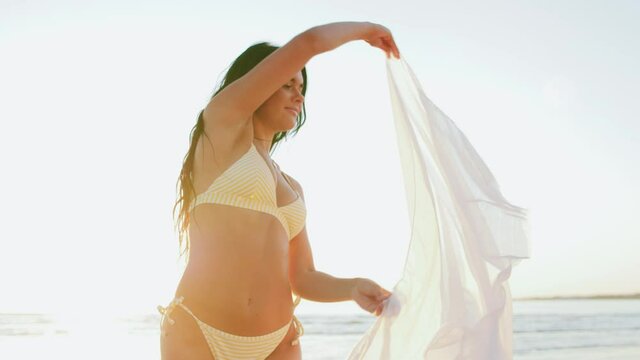 people, summer and swimwear concept - happy smiling young woman in bikini swimsuit with pareo on beach