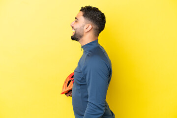 Young cyclist arab man isolated on yellow background laughing in lateral position