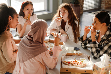 Multiracial young women eating pizza while having break