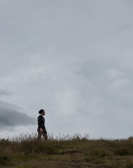 1 hombre caucásico con pelo largo y ropa negra parado en el césped mirando el horizonte (fotografía minimalista)