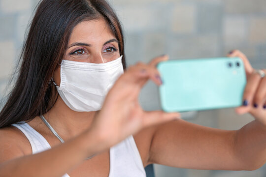 Young woman wearing surgical face mask using mobile smartphone  Girl in quarantine..Having fun video calling parents - Corona virus confinement and Youth millennial people concept