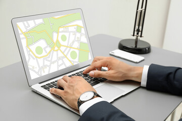 Man analyzing cadastral map on laptop at table, closeup