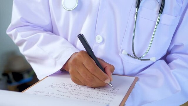 Doctor in uniform writing a short note and making doctor order after examining in clinic. 4K