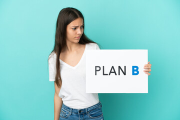 Young French woman isolated on blue background holding a placard with the message PLAN B with sad expression