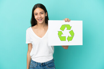 Young French woman isolated on blue background holding a placard with recycle icon with happy expression