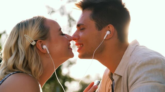 summer holidays, technology and people concept - happy couple with smartphone and earphones listening to music and kissing outdoors