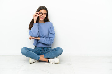 Young French girl sitting on the floor with glasses and happy