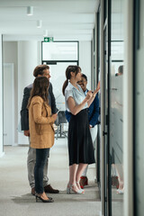 Group of Business People Analyzing Graph in Office Hallway.
Team of four multi-ethnic employee talking about business report while standing and working together in modern office corridor.