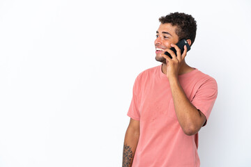 Young handsome Brazilian man isolated on white background keeping a conversation with the mobile phone with someone