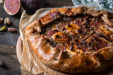 French galette with figs, goat cheese, pistachios and natural honey on baking paper on wooden...