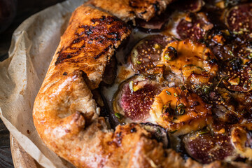 French galette with figs, goat cheese, pistachios and natural honey on baking paper on wooden table. 