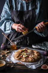 Process of making French galette with figs, goat cheese, pistachios and natural honey on baking paper on wooden table. 