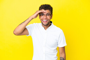 Fototapeta na wymiar Young handsome Brazilian man isolated on yellow background looking far away with hand to look something