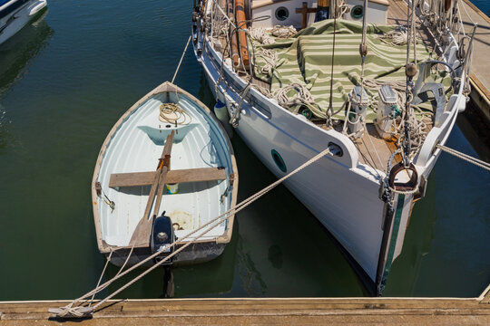 A small row boat tied next to the bow of a large yacht