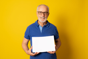 Great Offer. Cheerful Elderly Man Holding Blank Board For Text Standing Over yellow Studio Background. Panorama, Mockup