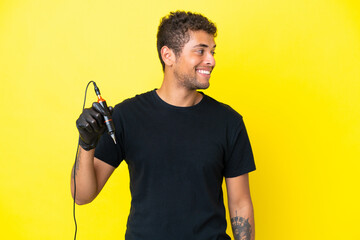 Tattoo artist Brazilian man isolated on yellow background looking to the side and smiling
