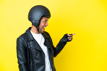 Young Brazilian man with a motorcycle helmet isolated on yellow background pointing finger to the side and presenting a product