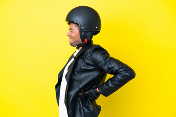 Young Brazilian man with a motorcycle helmet isolated on yellow background suffering from backache...