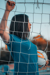 Chica jugadora de futbol agarrando la red sentada con el balon posando en la pista de juego