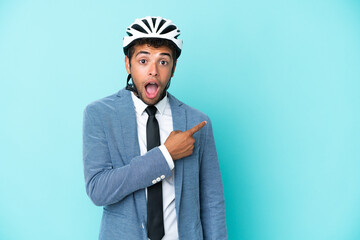 Young business Brazilian man with bike helmet isolated on blue background surprised and pointing side