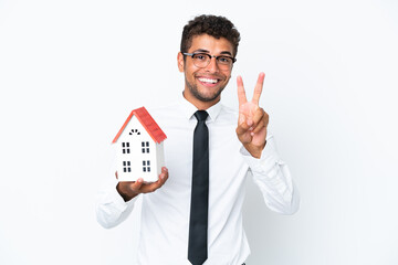 Fototapeta na wymiar Young business Brazilian man holding a house toy isolated on white background smiling and showing victory sign