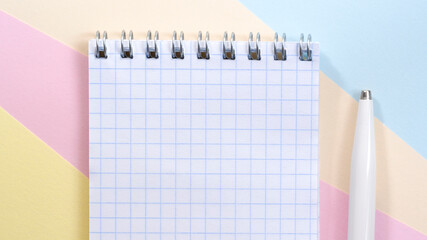 Education concept. Blank checkered page of notebook and White Pen on Multi colored paper geometric background.