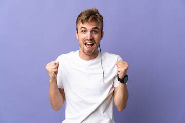 Young handsome blonde man isolated on purple background celebrating a victory in winner position