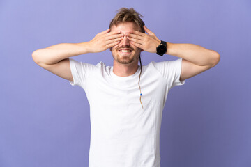 Young handsome blonde man isolated on purple background covering eyes by hands and smiling