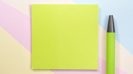 A Green Olive square blank piece of paper lies on a multi-colored background, next to it lies a Green pen.
