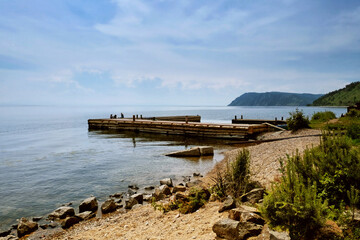 Obraz premium Idyllic view of the wooden pier in the lake with mountain scenery background. Lake Baikal in the day