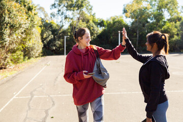 horizontal photo of two young women wearing coat and jacket holding each others hands on a sunny day